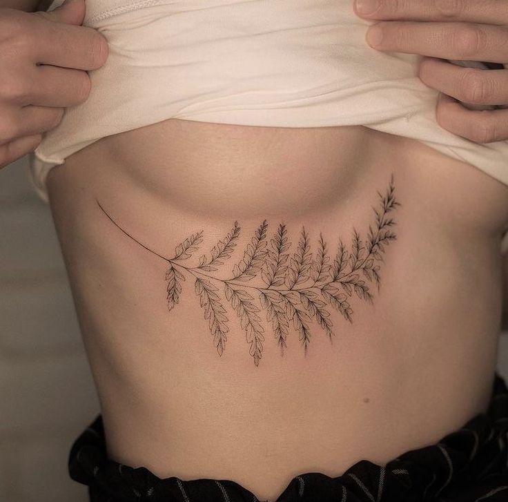 a woman's stomach with a fern leaf tattoo on her side ribcage