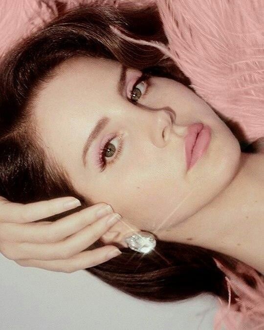 a woman laying down with her hand on her face and wearing a pink feathered dress