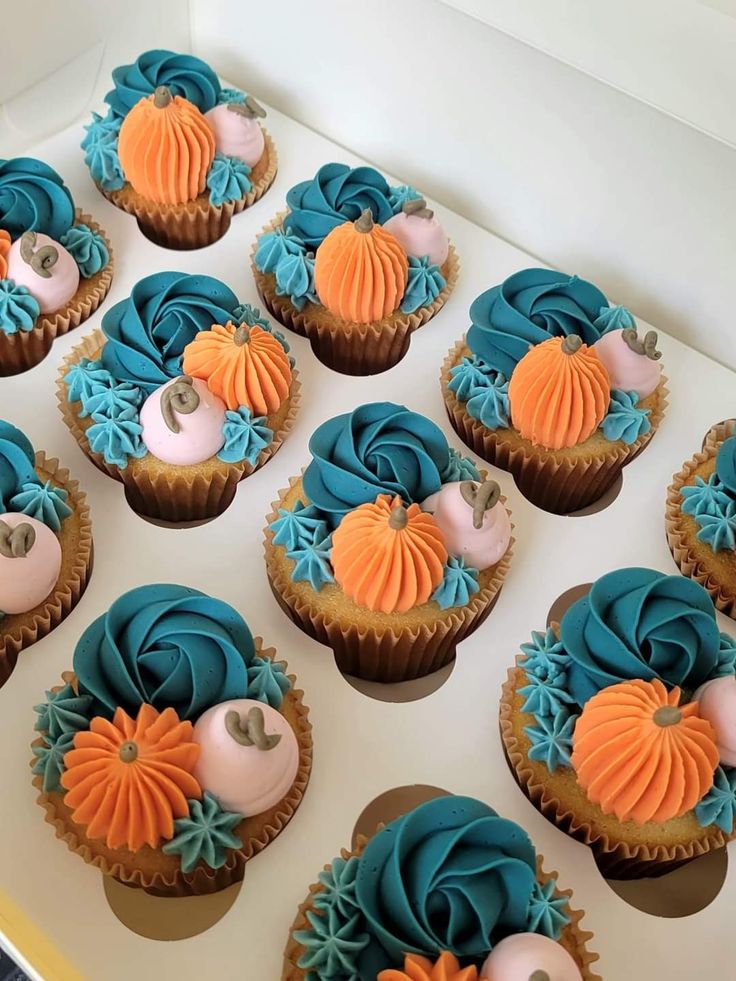 cupcakes with blue and orange frosting are arranged on a white table top