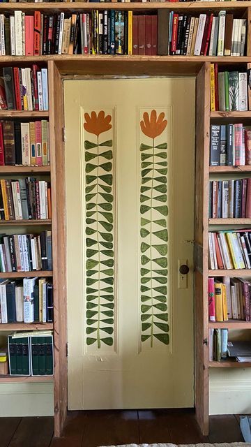 an open bookcase filled with lots of books next to a door that has flowers painted on it