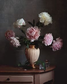 a vase filled with pink and white flowers on top of a wooden table next to a dresser