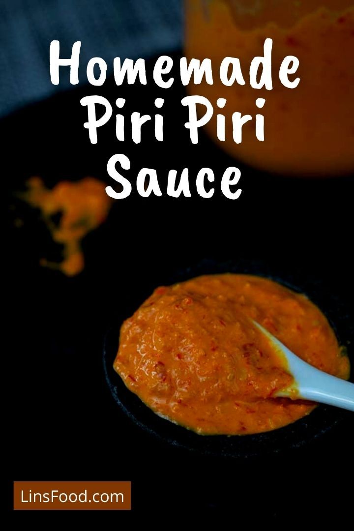 homemade piri sauce in a small black bowl with a spoon on the side and an orange jar behind it