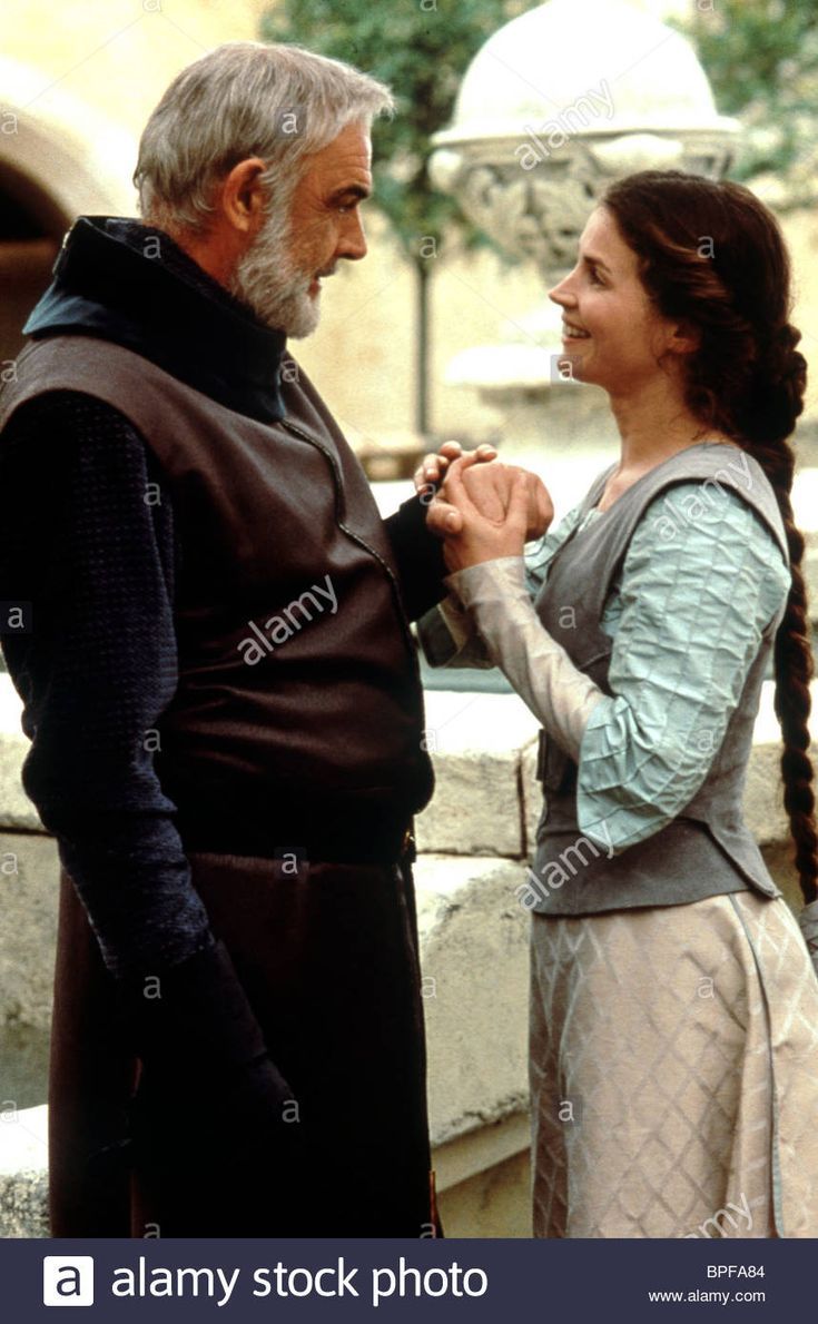 an older man and young woman standing next to each other in front of a fountain