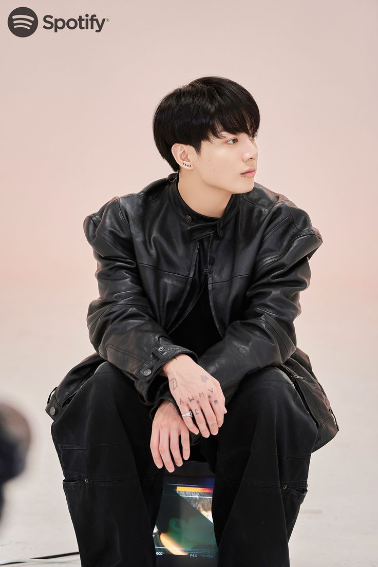 a young man sitting on top of a wooden bench wearing a black jacket and pants