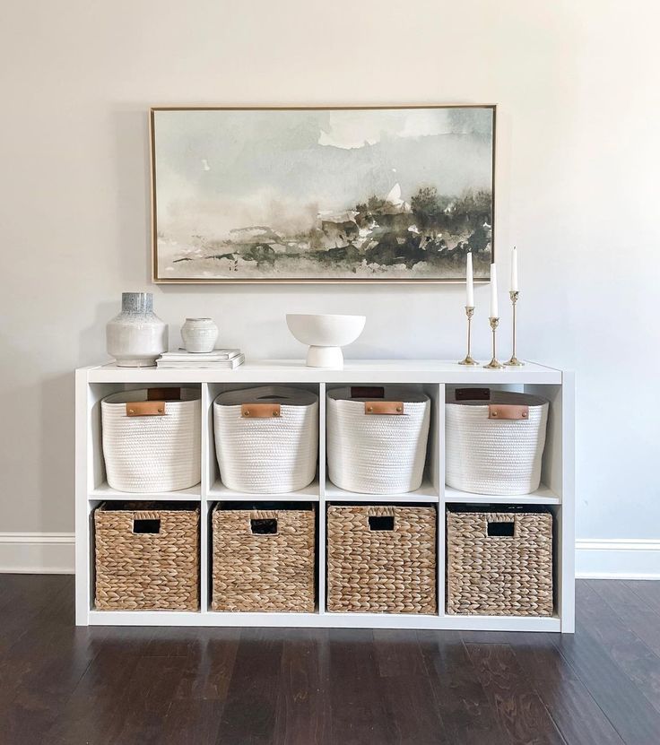 a white shelf filled with baskets next to a painting