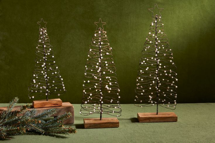 three small christmas trees sitting next to each other on top of a green tablecloth