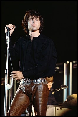 a man holding a microphone on stage with other people in the background at a concert