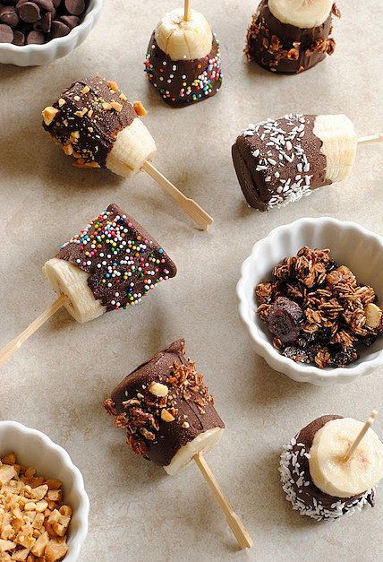 chocolate covered banana pops with sprinkles and other toppings on a table