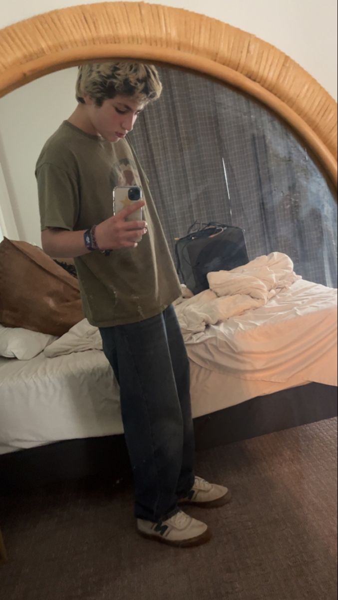 a young man standing in front of a mirror holding a water bottle and looking at his cell phone