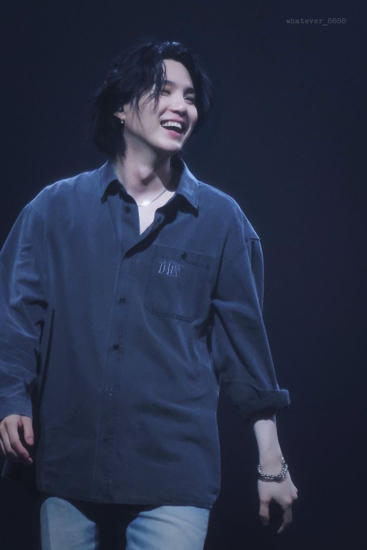 a man with black hair is smiling and wearing a blue button up shirt on stage