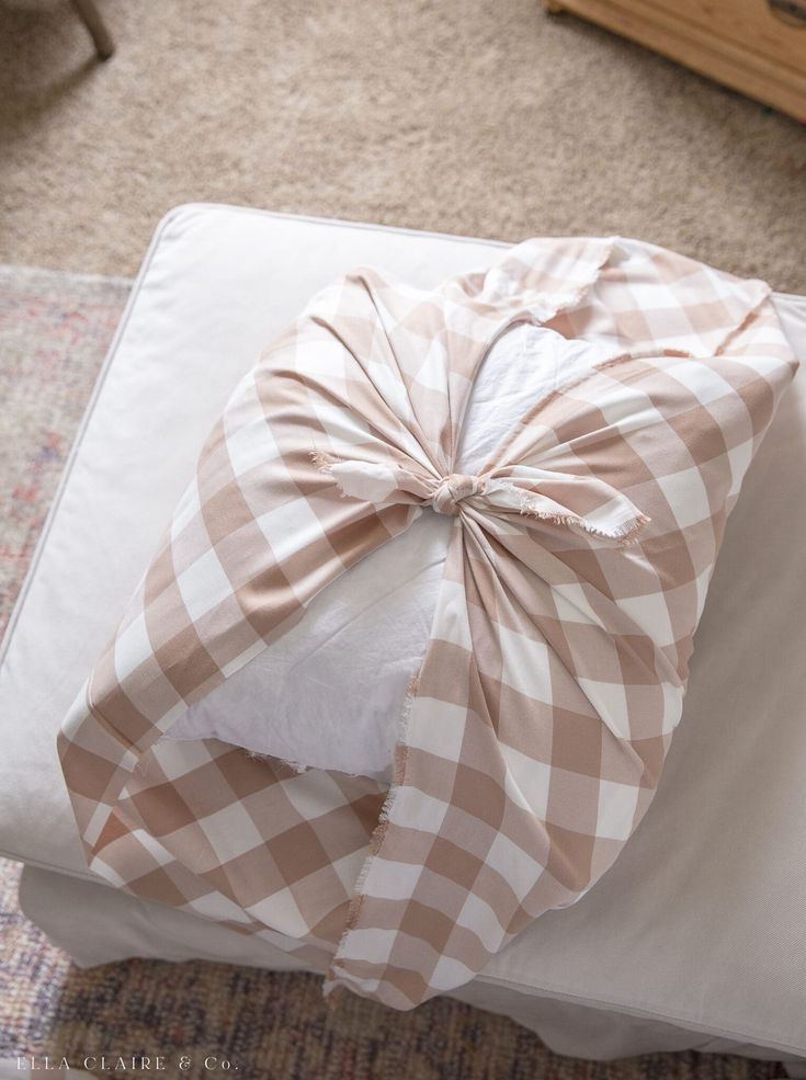 a wrapped present sitting on top of a white pillow covered in a brown and white checkered bow