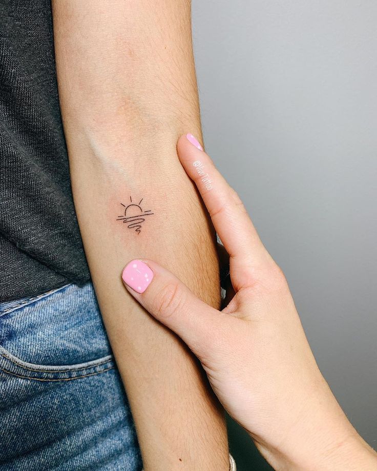 a woman's arm with a small sun tattoo on the left side of her arm