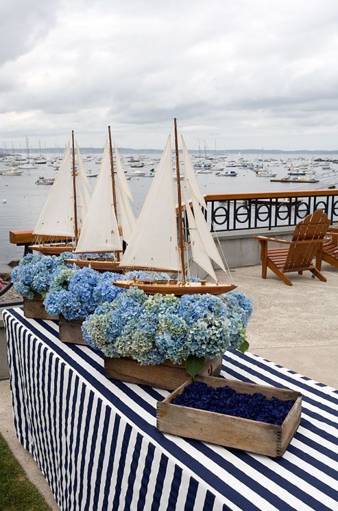 three wooden boats with blue flowers in them sitting on a table next to the water