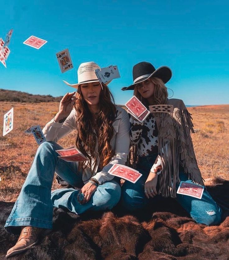 two women sitting on the ground with cards flying in the air above their heads and legs