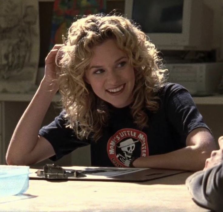 a woman sitting at a table with her hands on her head and smiling for the camera