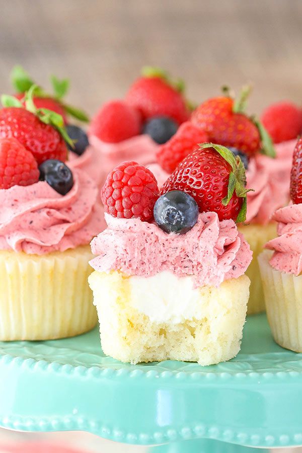 some cupcakes with pink frosting and berries on top are sitting on a blue plate