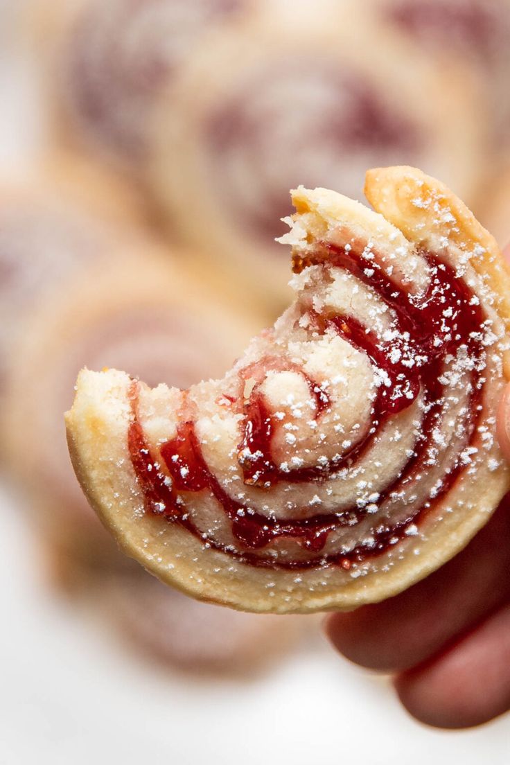 a hand holding up a pastry with powdered sugar on it