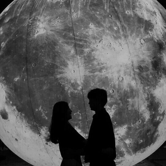 two people standing next to each other in front of the moon