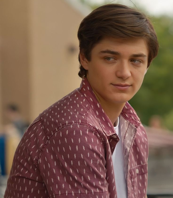 a young man wearing a red shirt and tie looking at the camera with a serious look on his face