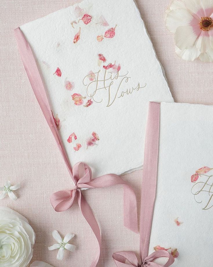 two wedding cards with pink ribbons and flowers on the table next to eachother