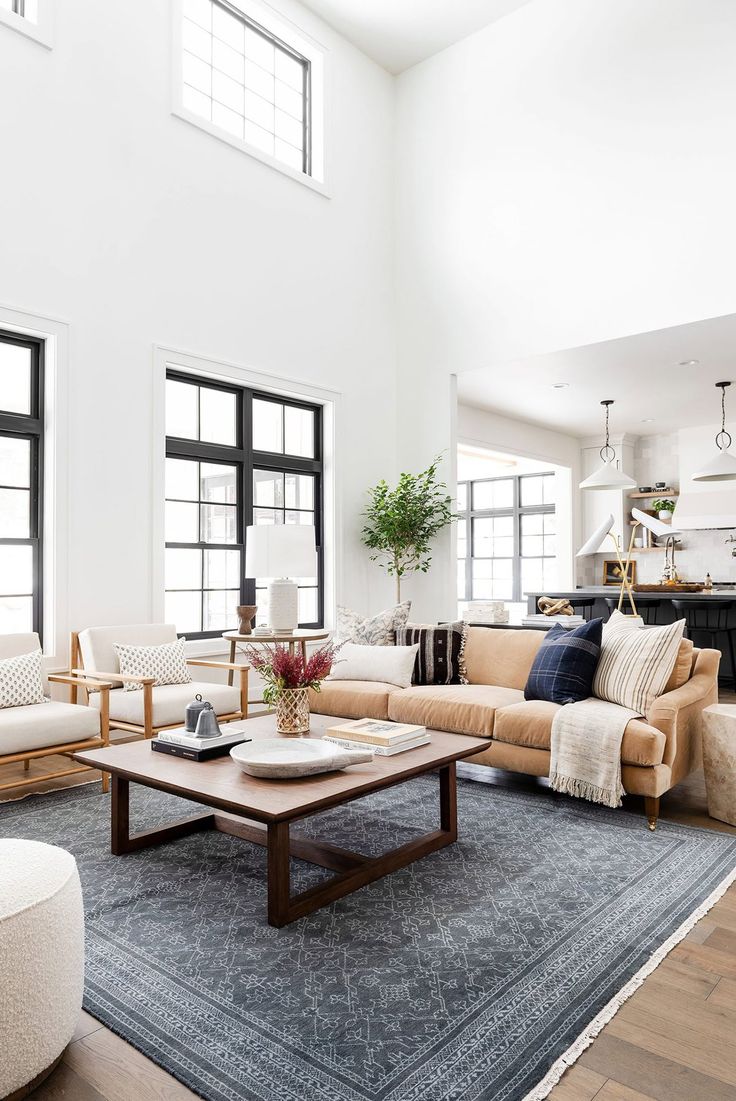 a living room filled with lots of furniture next to two large windows and a rug on the floor