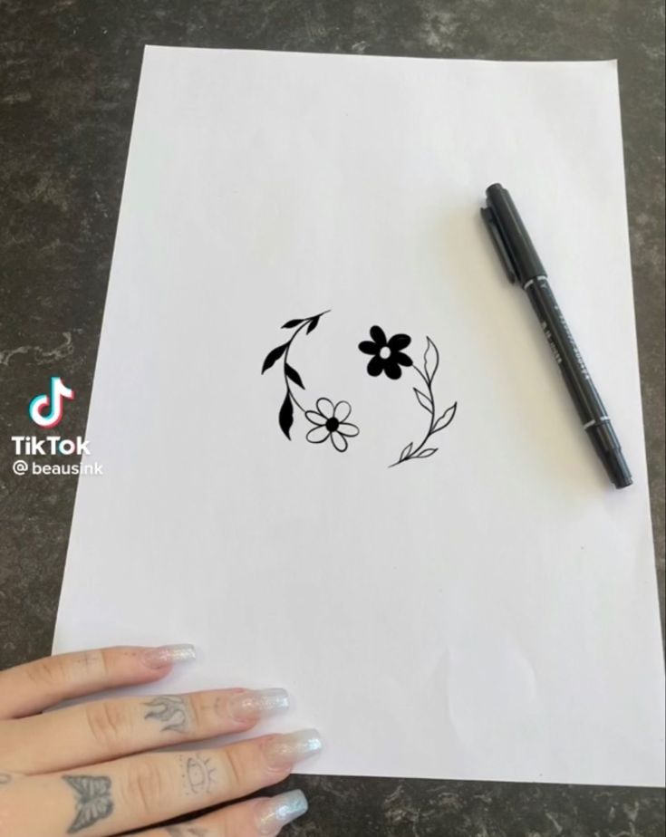 a person holding a pen next to a piece of paper with flowers drawn on it