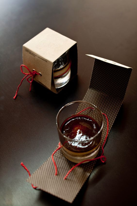 an empty glass cup sitting on top of a table next to a cardboard box and red string