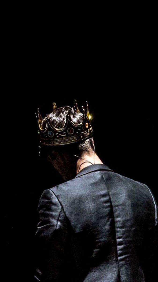 a man with a crown on his head looking down at something in the dark behind him