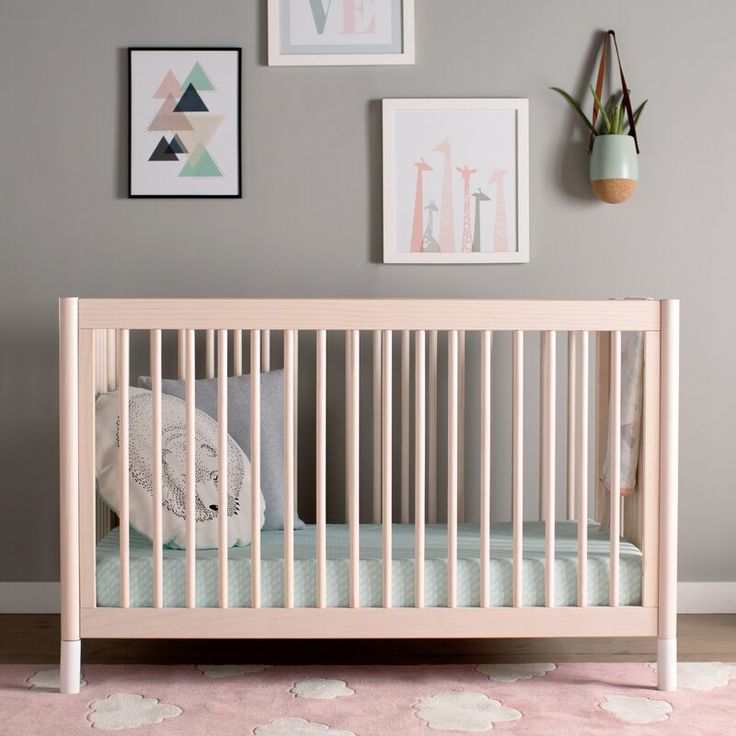 a baby crib in a room with pictures on the wall and pink rugs