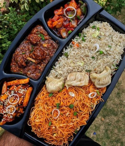 a person holding a tray with different types of food in it, including noodles and meats