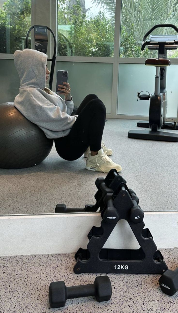 a person sitting on an exercise ball while using a cell phone in the gym area