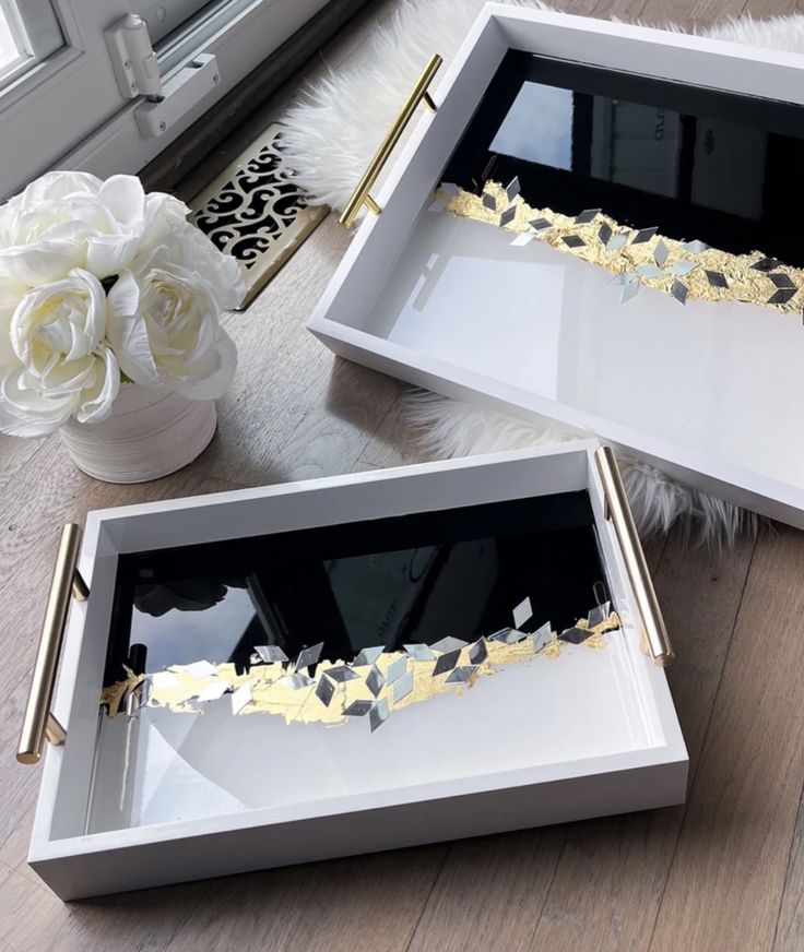 two white and gold serving trays sitting on top of a wooden floor next to a window