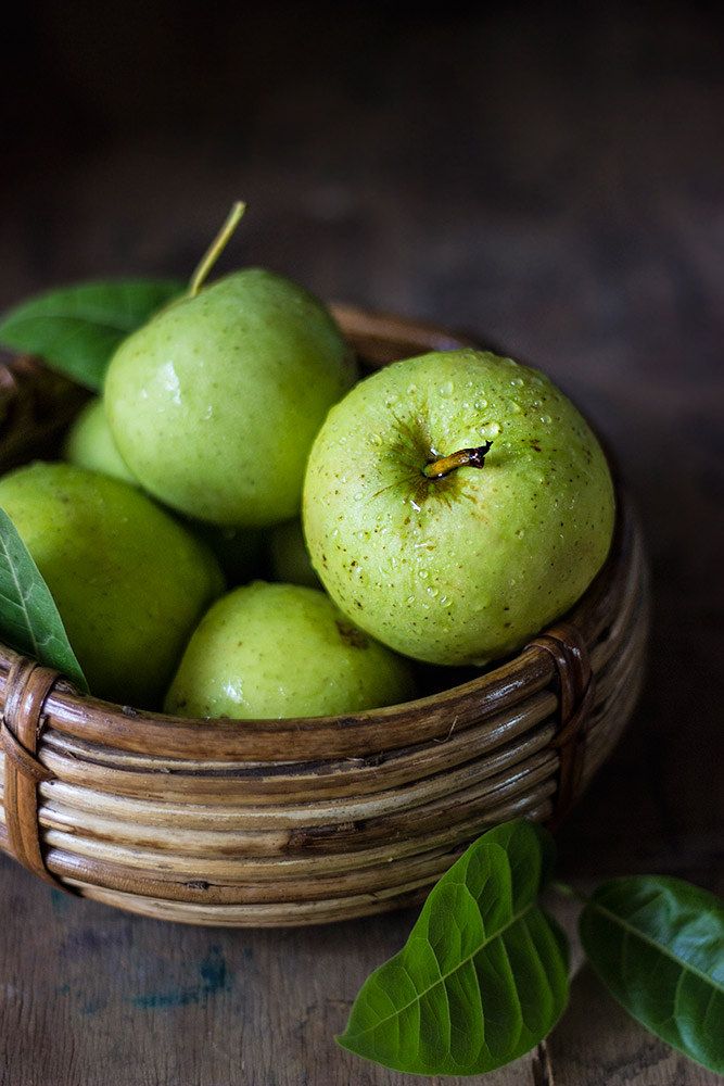 a basket filled with green apples sitting on top of a wooden table next to leaves