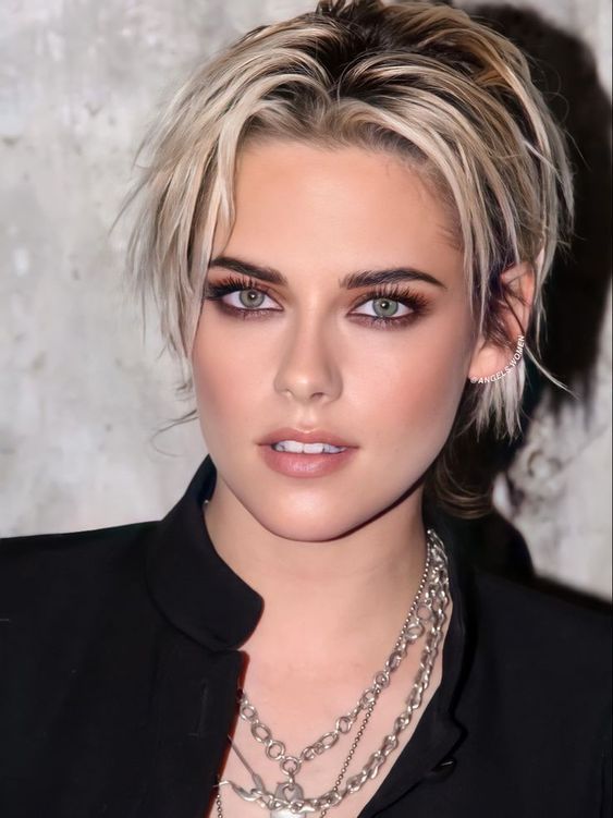 a woman with blonde hair wearing a black shirt and silver necklace, looking at the camera