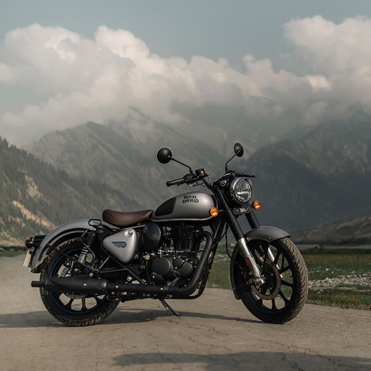 a motorcycle parked on the side of a dirt road in front of mountains and clouds