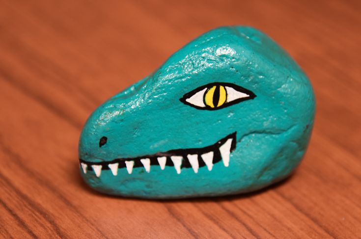 a rock with a painted dinosaur's face on it sitting on a wooden table