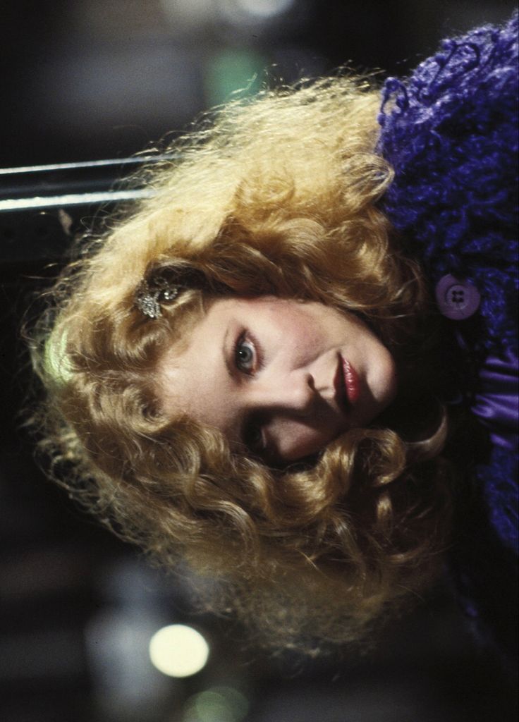 a close up of a person wearing a purple dress and posing for the camera with her hair blowing in the wind