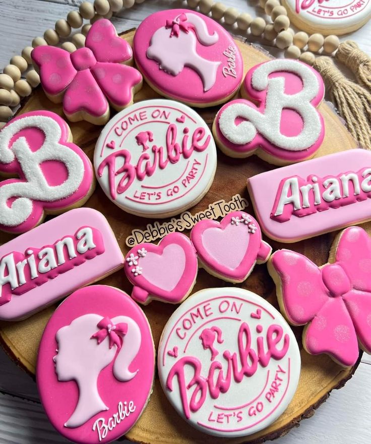 some decorated cookies are sitting on a wooden platter with pink and white icing