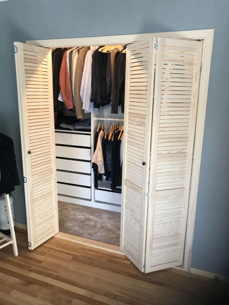 an open closet with white shutters and clothes hanging on hangers in the corner