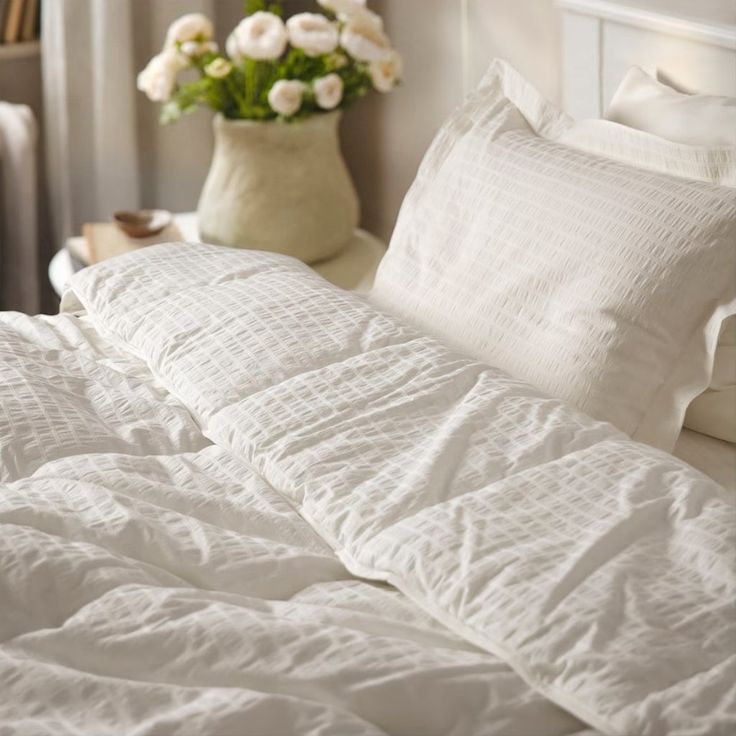 a bed with white linens and pillows in a bedroom next to a vase filled with flowers