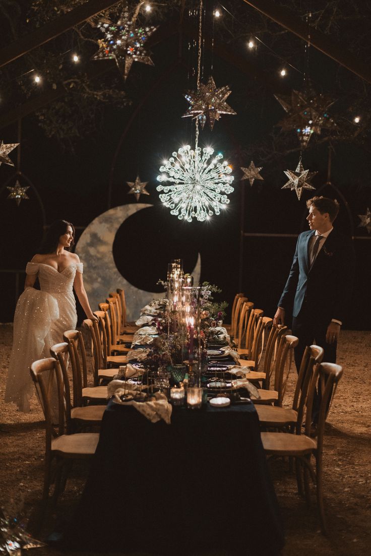 a couple standing next to each other in front of a long table with candles on it