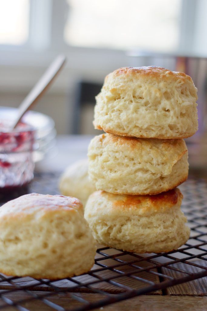 three biscuits stacked on top of each other next to a bowl of jam and a spoon