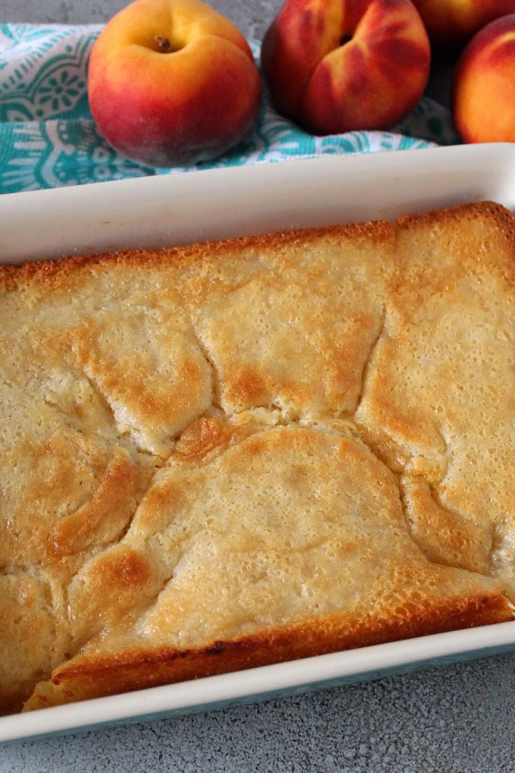 a white casserole dish filled with bread and peaches next to some apples