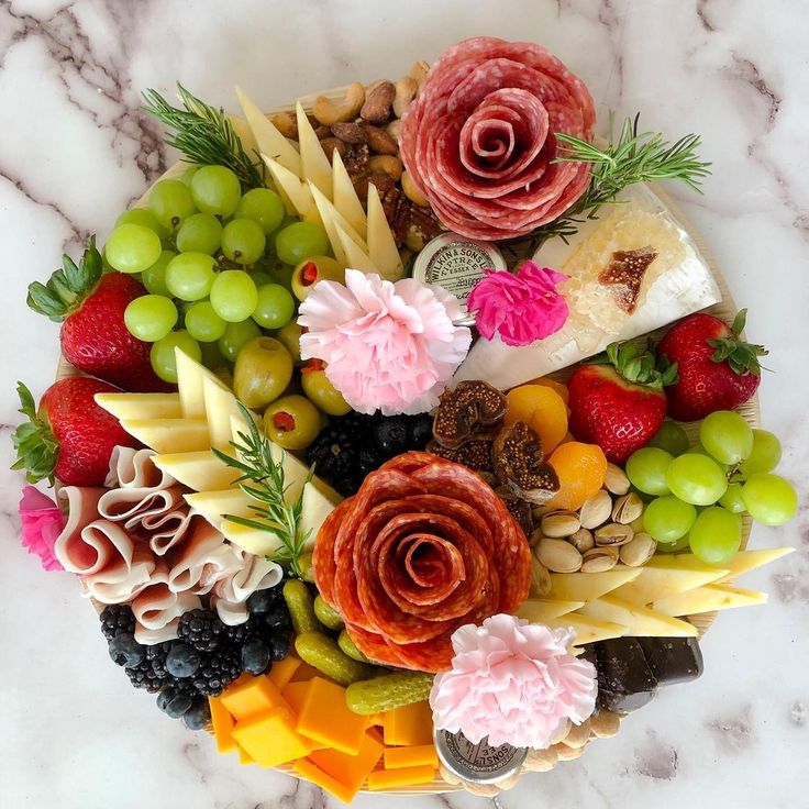 a platter filled with different types of cheeses and fruits on top of a marble table