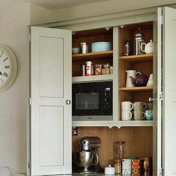 an open cabinet in the corner of a kitchen with a clock on the wall above it