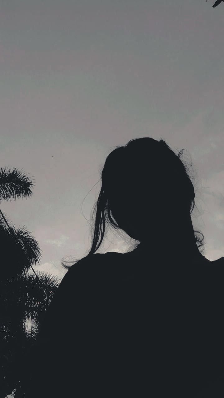 the silhouette of a woman with her hair blowing in the wind, looking up at an airplane flying overhead