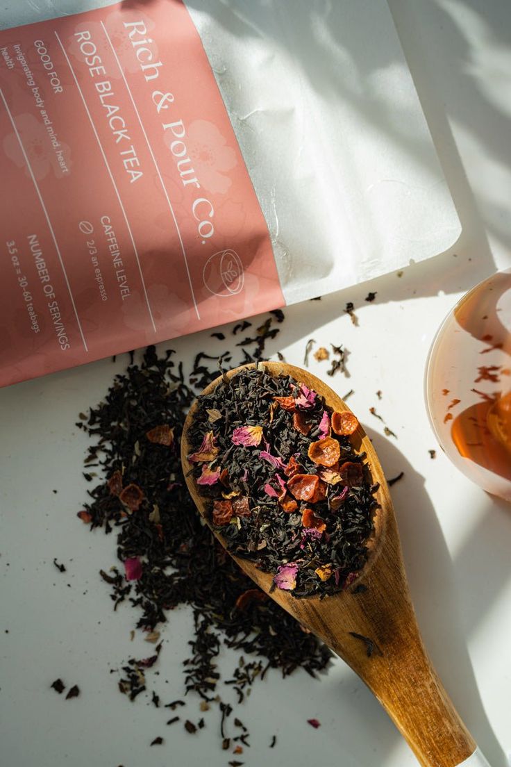 a wooden spoon filled with tea next to a bag of loose black tea and some other items