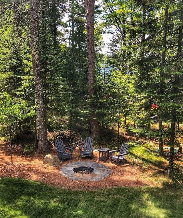 a fire pit in the middle of a forest with chairs around it and trees surrounding it