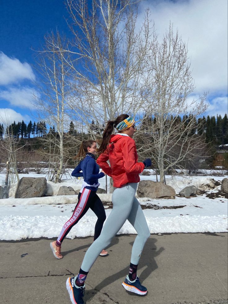 two people running in the snow near some trees