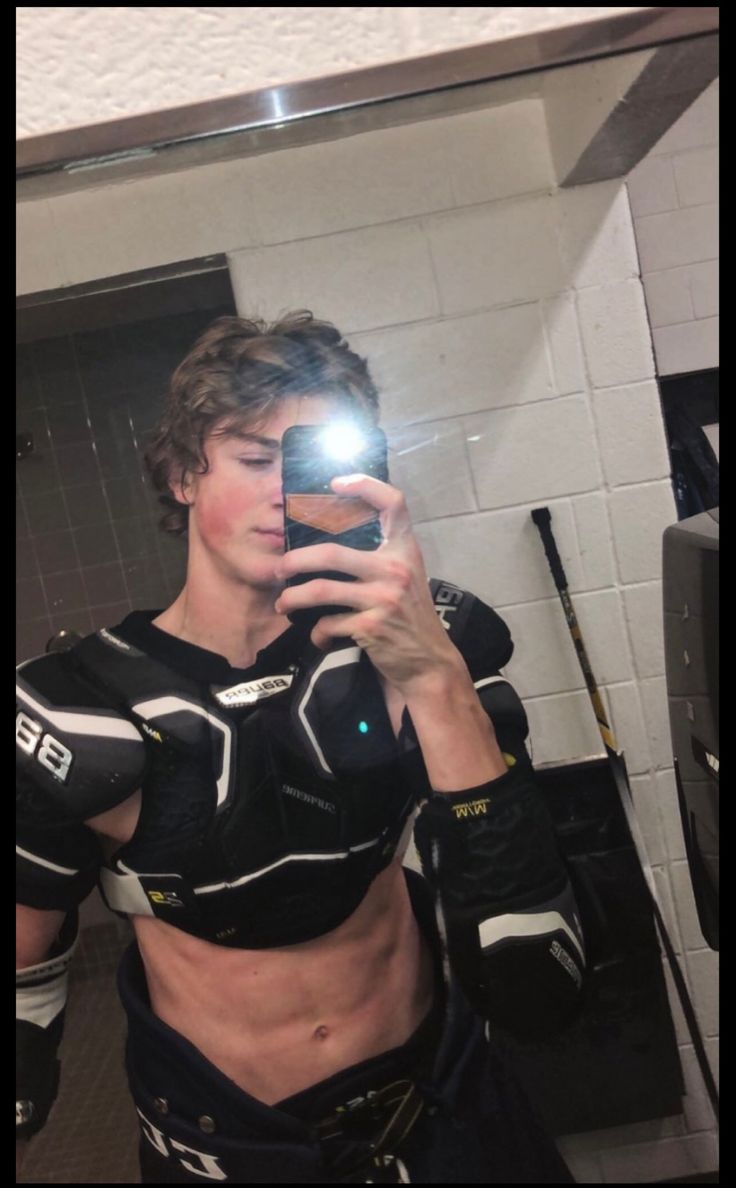 a man taking a selfie in the mirror with his cell phone while wearing a hockey uniform